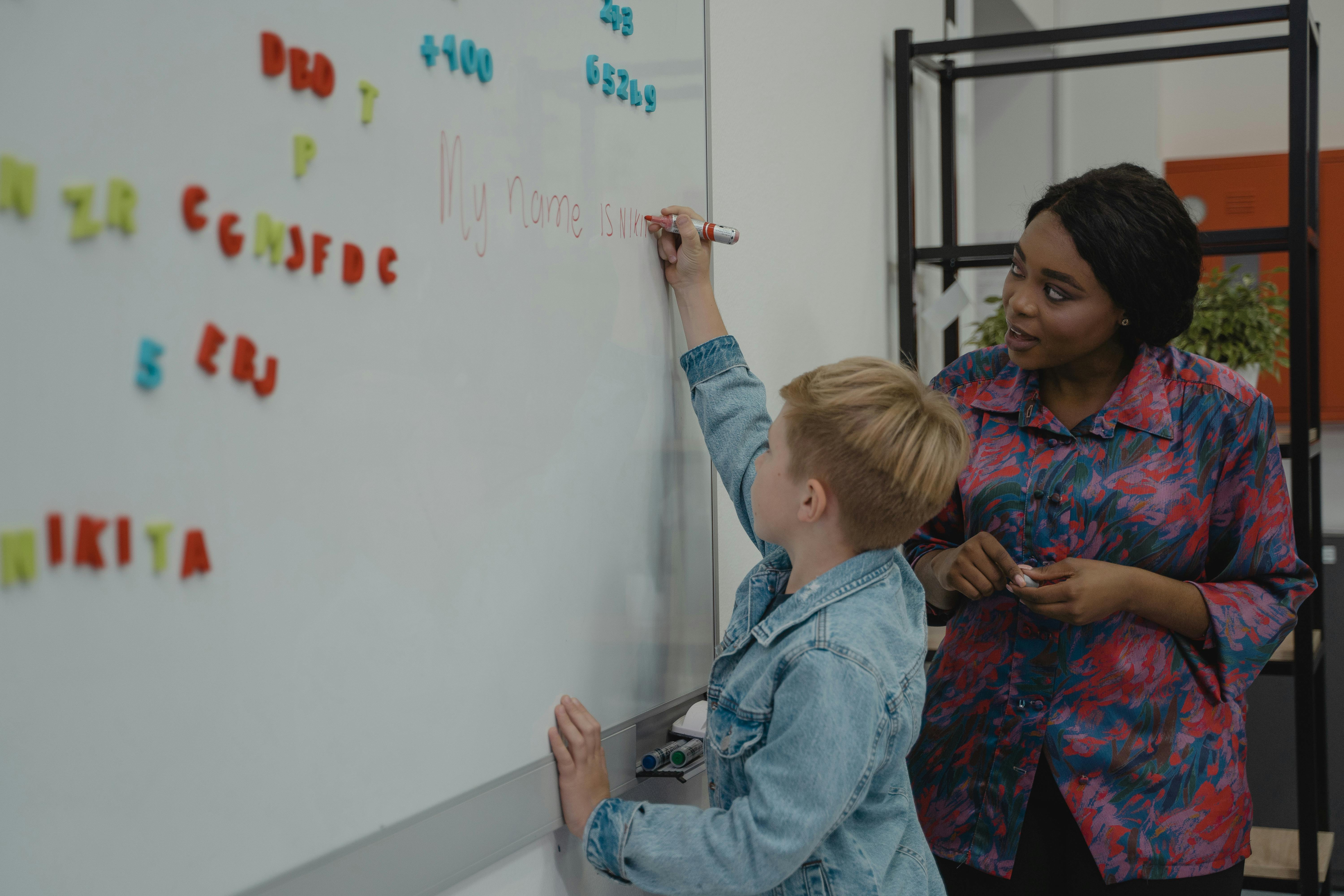 Teacher helps student write his name on board. 7 challenges of teaching.
