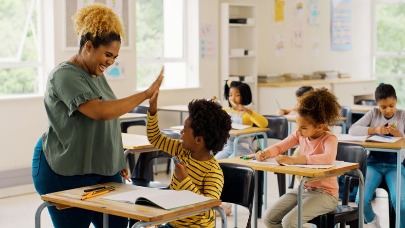 Teacher high-fives young student in class. Educational jargon for teachers to know. 