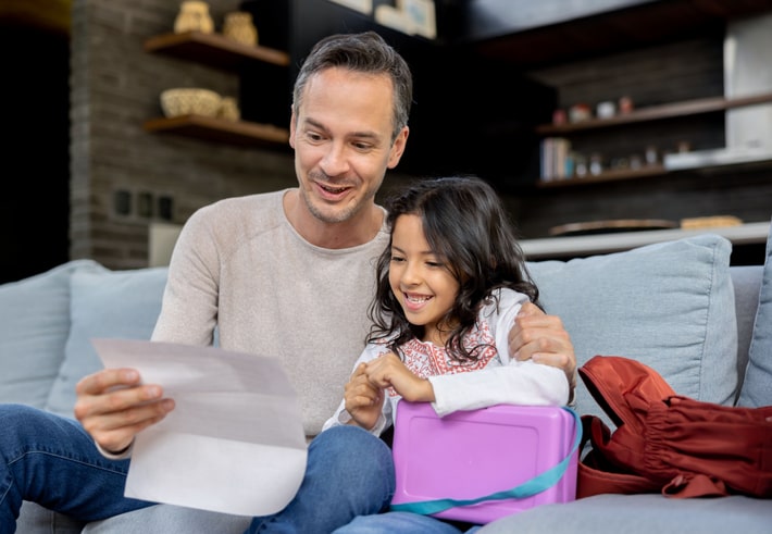 Father looking very happy looking at his daughter's grades at home. Report card advice for parents. 